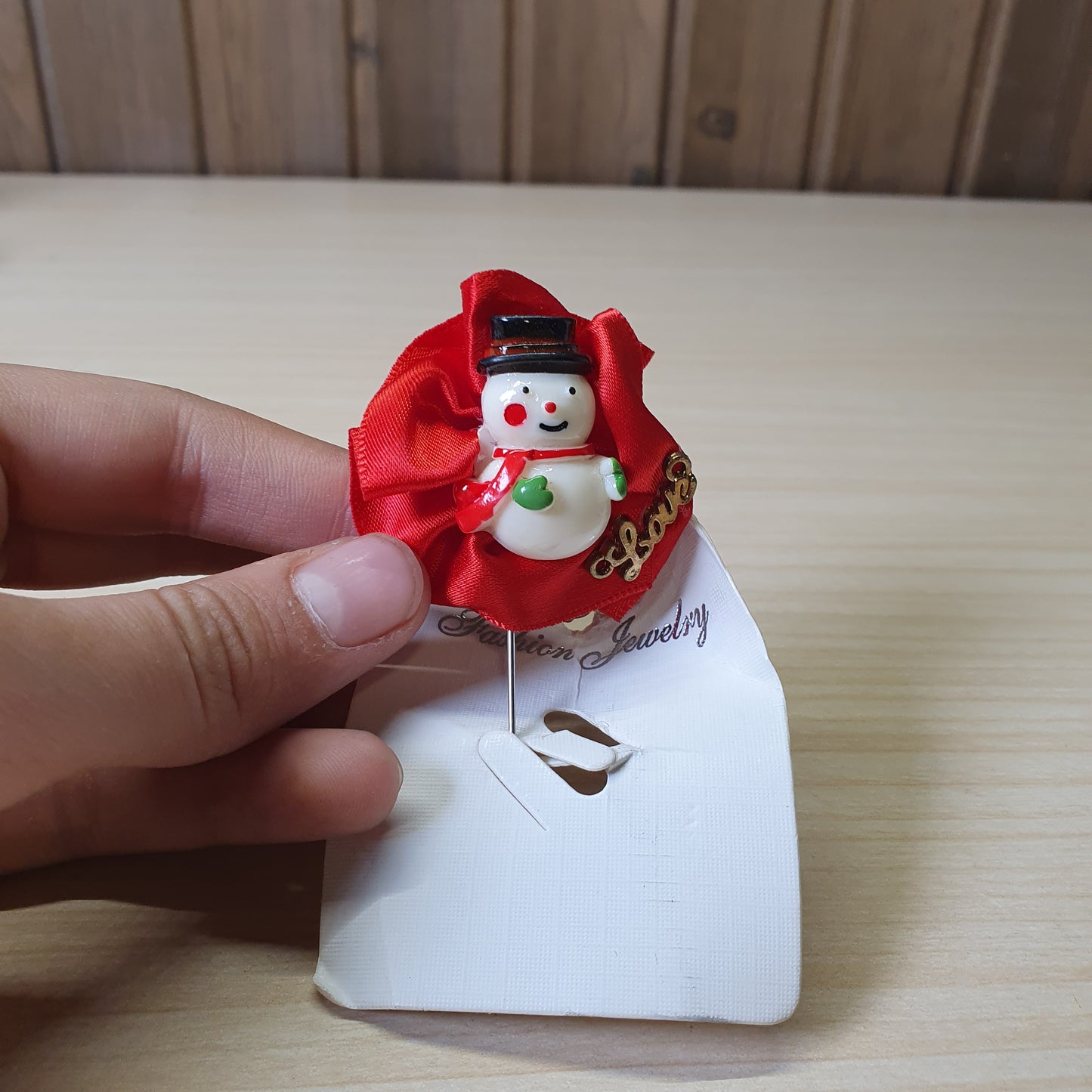 Festive snowman brooch by Fashion Jewelry features a central snowman figure against a bright red ribbon backdrop. #6856