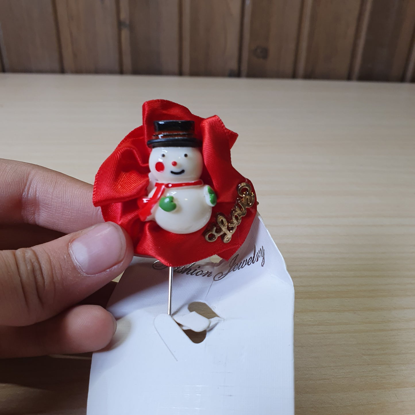 Festive snowman brooch by Fashion Jewelry features a central snowman figure against a bright red ribbon backdrop. #6856