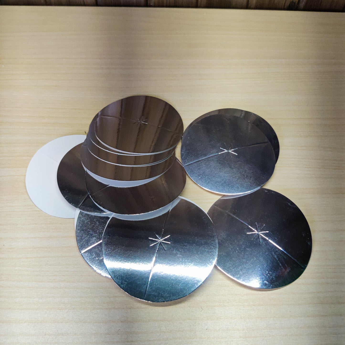 Silver-colored, circular candle drip protector disks made of aluminized paper.#2742
